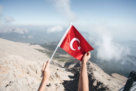 Turkey flag in a female hand against the backdrop of Taurus Mountains from a viewpoint of Tahtali Mountain. Tahtali Dagi, Antalya Province, Turkeyの写真素材