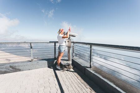Young woman tourist stands on a viewing platform of Tahtali Mountain in Kemer with a red Turkey flag and looks in binoculars, Turkeyの写真素材