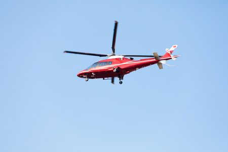 Side view of small red private helicopter against a blue sky with spinning propellersの写真素材