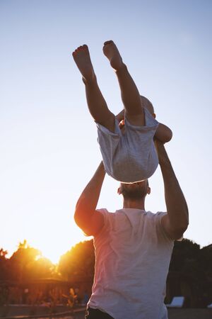 Father and son having fun on the beach against the setting sun. Father throws his child upの写真素材