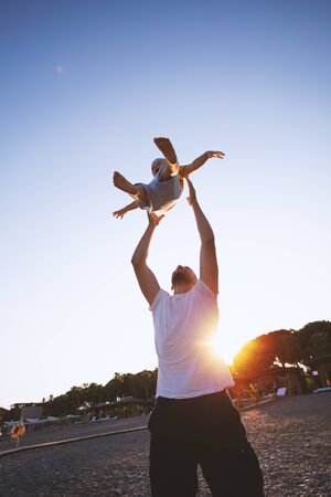Father and son having fun on the beach against the setting sun. Father throws his child upの写真素材