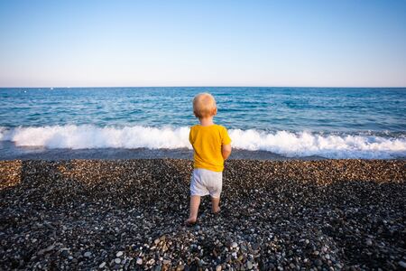 Little boy is throwing pebbles and stones into the sea.の写真素材