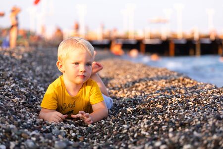 The boy lies on a pebble beach and looks at the seaの写真素材