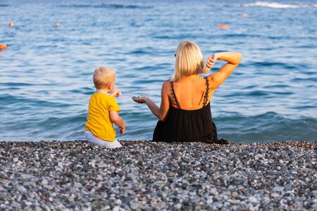 Mother and son throw pebbles into the water on the beach at sunsetの写真素材