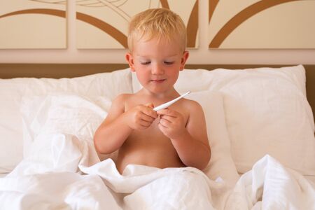 The boy sits in bed holds a thermometer in his handsの写真素材