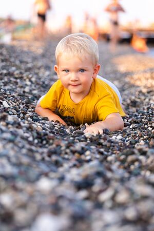 The boy lies on a pebble beach and looks at the seaの写真素材