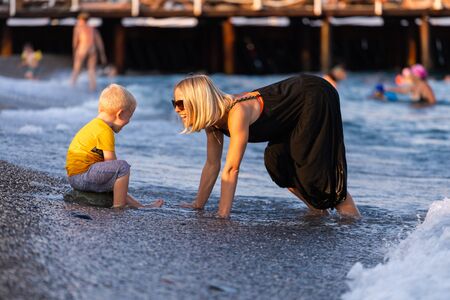Mother and her little son having fun on the beach at sunset during their vacationの写真素材