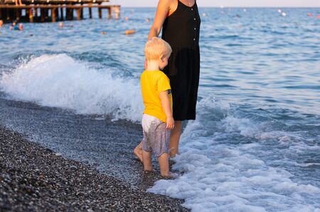 Mother and her little son walk along the coastline during their vacation and have fun at sunsetの写真素材