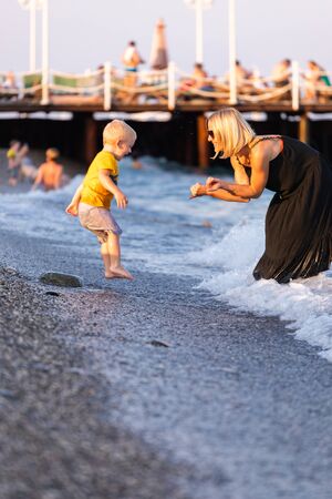 Mother and her little son having fun on the beach at sunset during their vacationの写真素材