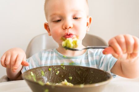 Little boy alone eats puree from a plate.の写真素材