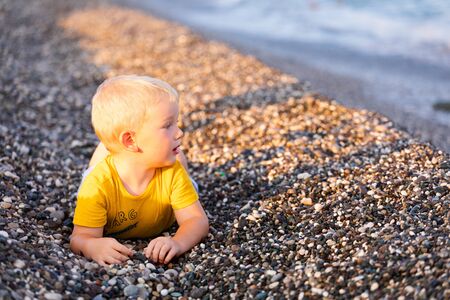 The boy lies on a pebble beach and looks at the seaの写真素材