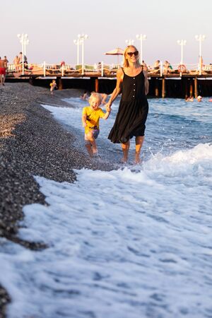 Mother and son strolling along the coastline at sunsetの写真素材