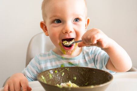 Little boy alone eats puree from a plate.の写真素材