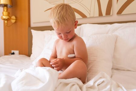 A little boy lies in his parent's bed and measures the temperature with an electronic thermometerの写真素材