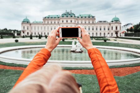 A young happy female tourist takes a photo against the backdrop of the Belvedere Palace in Vienna, Austriaのeditorial素材