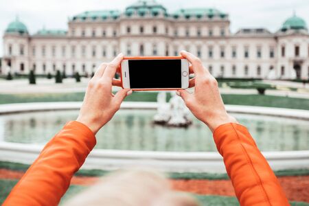 A young happy female tourist takes a photo against the backdrop of the Belvedere Palace in Vienna, Austriaのeditorial素材