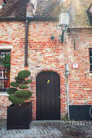 Beautifully decorated house entrance with red brick walls, a small black door and timber trees on the sides.の写真素材