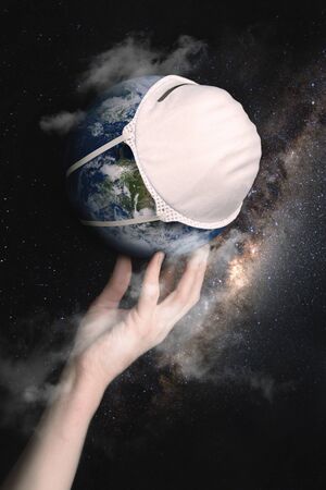 A female hand holds the globe with a medical mask during an epidemic of Covid 19 or coronavirus worldwide. Concept on a background of the starry sky with a milky way. Elements of this image are furnished by NASA.の写真素材