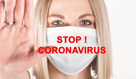 Close-up portrait of woman in medical mask with the inscription STOP Coronavirus with outstretched arm symbolizing the word STOP.の写真素材