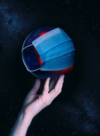 A female hand holds the globe with a medical mask during an epidemic of Covid 19 or coronavirus worldwideの写真素材