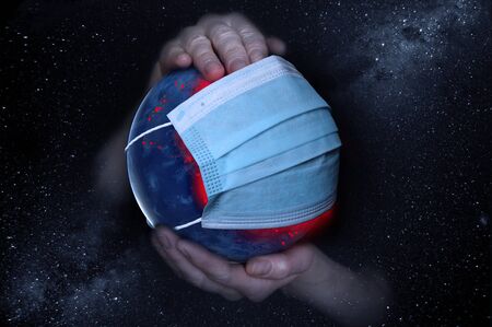Female hands hold the Earth in a medical protective mask against the starry sky during the epidemic Covid19 or coronavirus.の写真素材