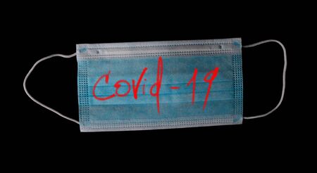Medical mask with the inscription Covid 19 isolated on blackの写真素材