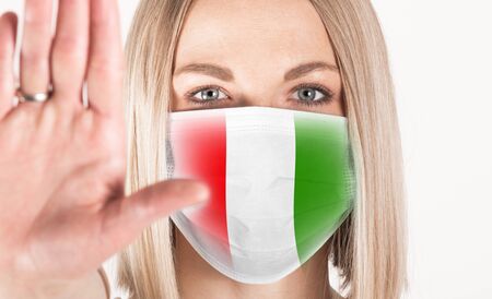 Close-up portrait of woman with flag of Italy on medical mask with outstretched arm symbolizing the word STOP.の写真素材
