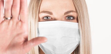 Close-up portrait of woman in medical mask with outstretched arm symbolizing the word STOP.の写真素材