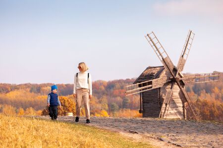 Mom and her child walk in the Pirogovo Museum in the fall against the background of an old mill and...