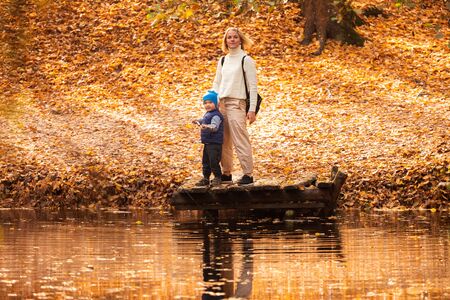 Happy young mother and her son spending time in the autumn park near the pond.の写真素材