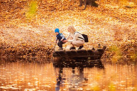 Happy young mother and her son spending time in the autumn park near the pond.の写真素材