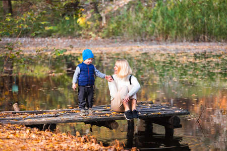 Happy young mother and her son spending time in the autumn park near the pond.の写真素材