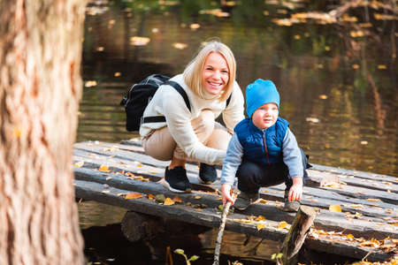 Happy young mother and her son spending time in the autumn park near the pond.の写真素材