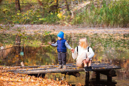 Happy young mother and her son spending time in the autumn park near the pond.の写真素材