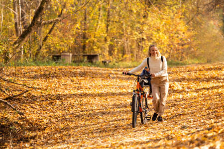 Happy mother leads a bicycle with a child strapped in the back in the autumn park.の写真素材