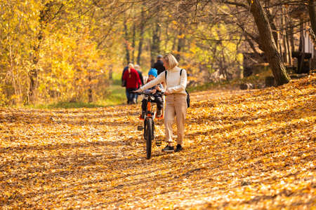 Happy mother leads a bicycle with a child strapped in the back in the autumn park.の写真素材