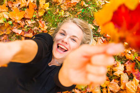 Woman lying on the grass with fallen orange leavesの写真素材