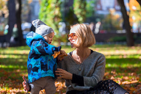 Mother and son are played in the fallen leaves for a walk in the city parkの写真素材