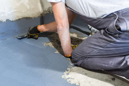 A builder worker applies a waterproofing mortar to the floor in a room.の写真素材