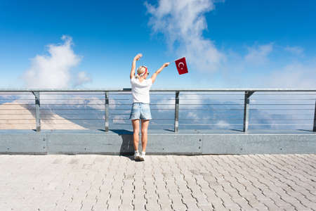 Young woman tourist stands on a viewing platform of Tahtali Mountain in Kemer with a red Turkey flag, Turkeyの写真素材