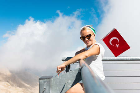 Young woman tourist stands on a viewing platform of Tahtali Mountain in Kemer with a red Turkey flag, Turkeyの写真素材