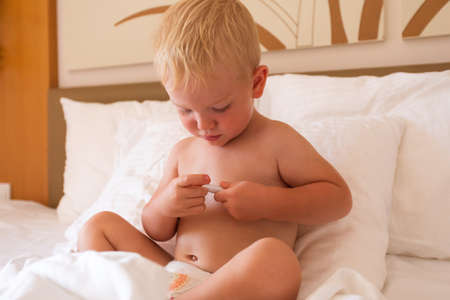 The boy sits in bed holds a thermometer in his handsの写真素材
