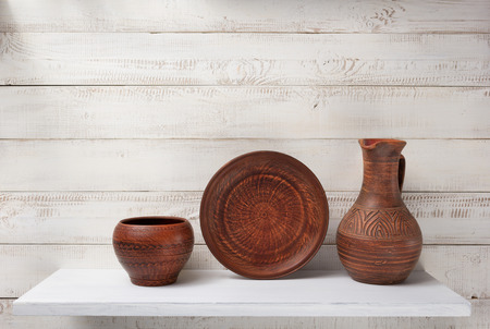 clay jug and plate at shelf on white wooden plank backgroundの写真素材