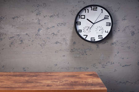 wall clock and table near concrete background, dark grey texture surface