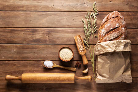 Loaf of fresh bread and bakery ingredients for homemade baking on wooden table. Baker food set at wood plank board background texture with copy space. Flat lay top viewの写真素材