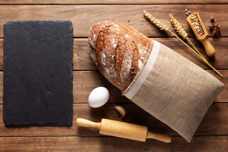 Loaf of fresh bread and bakery ingredients for homemade baking on wooden table. Baker food set at...