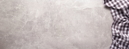 Folded checked or checkered tablecloth at stone surface of table. Top view as panorama of cloth...