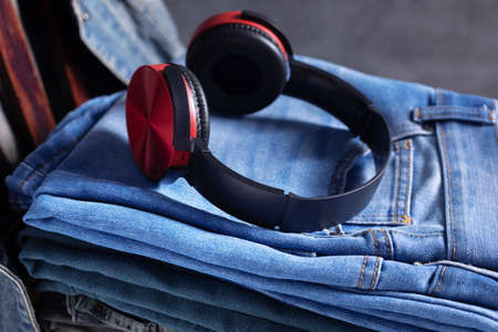 Denim jeans and earphones or headphones at old wooden chair near grey wall background texture. Front view of stack classic jeans fashionの写真素材