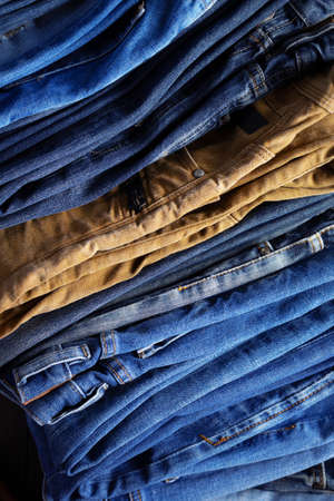 Stack or pile of denim jeans as background texture. Heap of folded jeans trousers