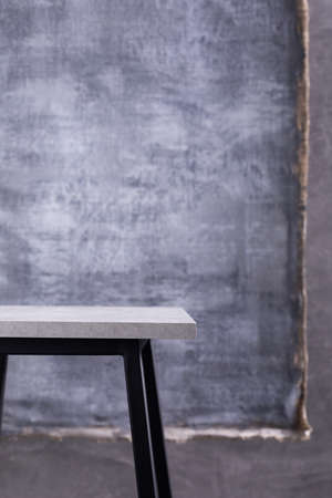 Table or metal stool and abstract painted canvas  near concrete wall background. Tabletop or shelf